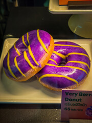 Colorful and eye-catching “Very Berrie” donuts on a white plate, displayed in a bakery with a price tag 