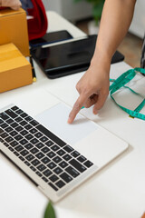 Person pointing at laptop touchpad on desk with boxes and measuring tape