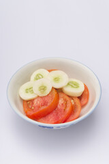 sliced tomato and sliced cucumber in a bowl on white background