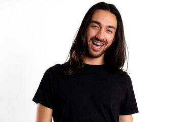 Young Latin man with long hair smiles with fixed braces on a white background with black clothes