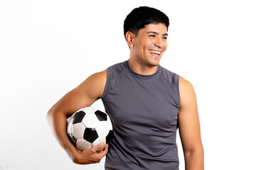 Young Latin man, dressed in sportswear, looks away and holds soccer ball under his arm