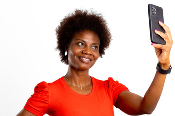 Young black woman, afro hair, smiles looking at phone in selfie on white background