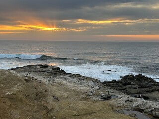 A vibrant sunset at Point La Jolla, California, features brilliant sun rays, with birds and sea lions peacefully resting on sun-kissed coastal rocks.