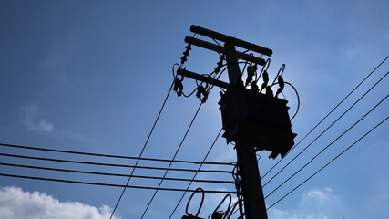 Silhouette of transformer on pole. Three-phase transformer with low voltage cable below with afternoon sun on blue sky background and copy space for text. selective focus