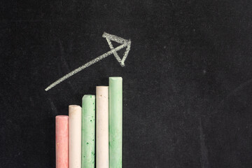 Color chalk sticks arranged as bar chart on blackboard with upward arrow symbolizing growth progress and success. 