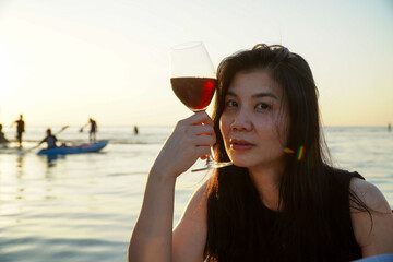 Woman drinking red wine on the beach at sunset. Beautiful asian woman drinking red wine on the beach.