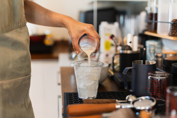 Woman barista preparing coffee latte pouring milk into a glass with iced.