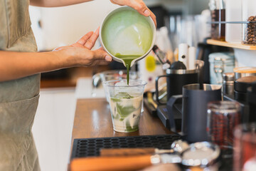 Woman barista pouring Matcha into glass with milk.