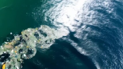 Aerial view of plastic pollution floating in ocean water near rocky coastline causing environmental damage and harm to marine life