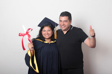 Proud and satisfied single dad with his brunette Latina daughter, a graduate dressed in a cap and...