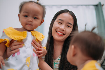 Selective focus shot, Young Asian mother shares a happy moment with her twin daughters while sitting on a soft carpet in a cozy room at home. Leisure activities with family