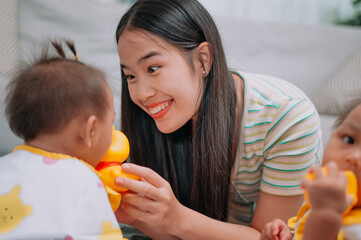 Selective focus shot, Young Asian mother shares a happy moment with her twin daughters while sitting on a soft carpet in a cozy room at home. Leisure activities with family