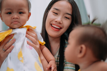 Selective focus shot, Young Asian mother shares a happy moment with her twin daughters while sitting on a soft carpet in a cozy room at home. Leisure activities with family