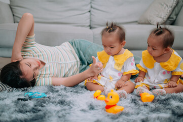 Portrait of Young mother lies on a carpet taking care of her twins while they play with toys in the living room at home.