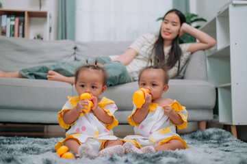 Portrait of Asian mother lies on the couch and takes care of her twins while they play with toys in the living room at home.
