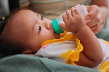 Selective focus shot, Asian mother feeding her baby with a bottle on the sofa in her living room at home. Take care of baby with love and care.