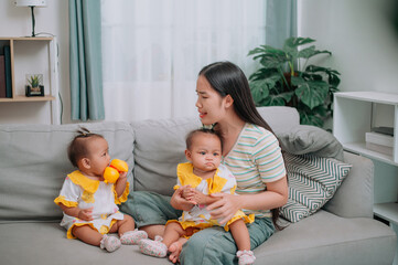 Portrait of Single mother spends happy time with her twin daughters in a warm room at home. Take care of baby with love and care.