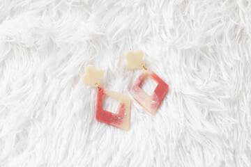 Geometric dangle earrings with red and beige color, modern acrylic jewelry on soft white fur background, stylish accessory for women, elegant and trendy fashion