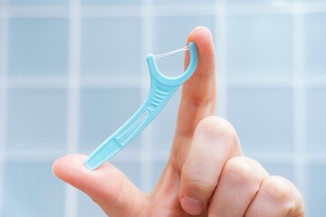 Female hand holding disposable dental floss close-up against the background of blue tiles in the...