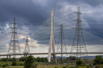 Flintshire Bridge stands prominently under a dark, cloudy sky, flanked by numerous large electricity pylons and their intricate web of power lines
