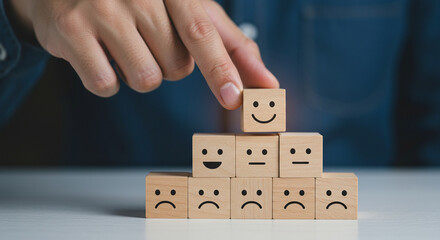 A hand placing a wooden block with a smiling face on top of a pyramid of emotion blocks on a table