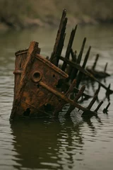 Selbstklebende Fototapeten Rusted ship wreck partially submerged in murky water with exposed wooden beams and metal hull decay © Hamidsheraz123