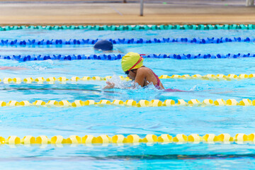 Swimmer child swims breaststroke swimming style in a race swimming pool. Water sports and competition, learning to swim classes for children.