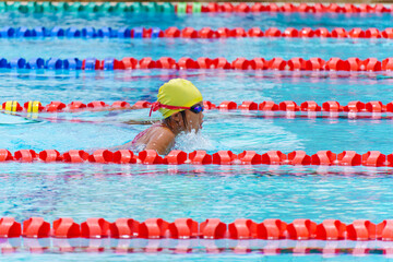 Swimmer child swims breaststroke swimming style in a race swimming pool. Water sports and competition, learning to swim classes for children.