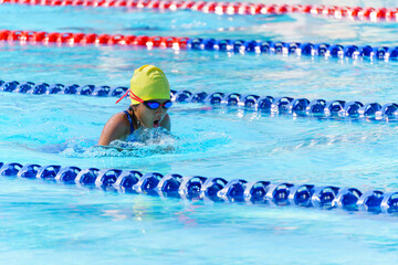 Swimmer child swims breaststroke swimming style in a race swimming pool. Water sports and competition, learning to swim classes for children.
