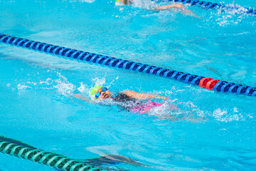 Swimmer child swims backstroke swimming style in a race swimming pool. Water sports and competition, learning to swim classes for children.