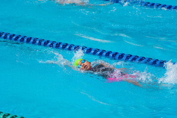 Swimmer child swims backstroke swimming style in a race swimming pool. Water sports and competition, learning to swim classes for children.