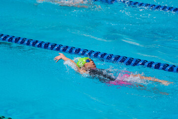 Swimmer child swims backstroke swimming style in a race swimming pool. Water sports and competition, learning to swim classes for children.