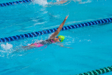 Swimmer child swims backstroke swimming style in a race swimming pool. Water sports and competition, learning to swim classes for children.