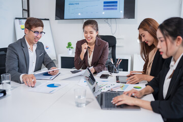 Group of Asian businesspeople sit at a table with graph paper in a meeting.