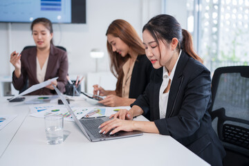 Group of Asian businesspeople sit at a table with graph paper in a meeting.	