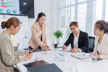 Group of Asian businesspeople sit at a table with graph paper in a meeting.