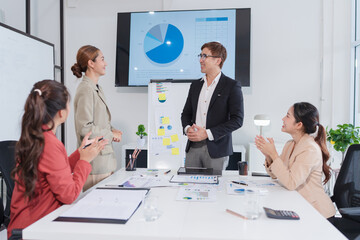 Group of Asian businesspeople sit at a table with graph paper in a meeting.