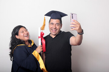 Proud and satisfied single dad with his brunette Latina daughter, a graduate dressed in a cap and...