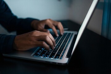 Hands Typing on Illuminated Laptop Keyboard in Dark Room Focus on Fingers and Keys Night Work