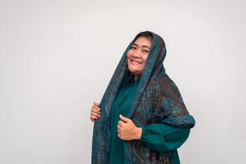Smiling woman in green dress and patterned shawl poses against w
