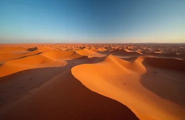 Fototapete Rund Panoramic view of Sahara desert sand dunes under blue sky. Orange sand waves. Desert landscape at sunrise. Merzouga Morocco travel destination. Sandy terrain. Adventure tourism. © Maryna