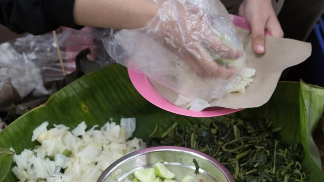 A close-up of a street vendor preparing pecel, a traditional Indonesian salad made from blanched vegetables served with peanut sauce.