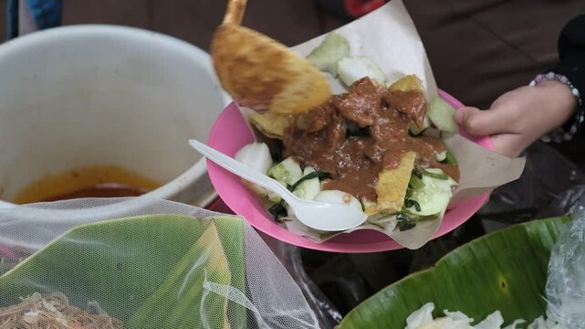 A close-up of a street vendor preparing pecel, a traditional Indonesian salad made from blanched vegetables served with peanut sauce.