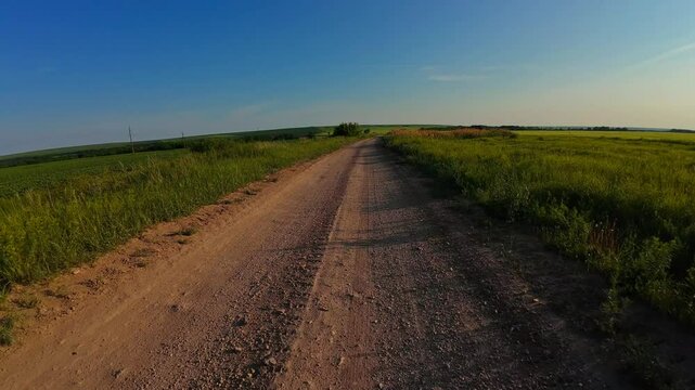 Cycling on a dirt country road in summer in a field at sunset