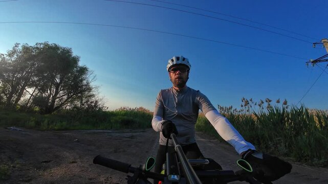 man riding bike at sunset outside city and filming video for blog, solo bike trip