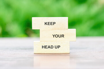 Concept words KEEP YOUR HEAD UP painted on wooden blocks on a bright green background, reflecting...