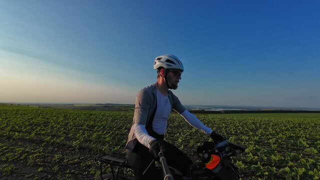 man riding bike at sunset outside city and filming video for blog, solo bike trip