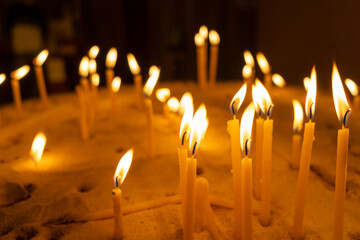 Burning candles with warm flames placed in a bed of sand