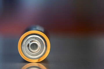 One AA alkaline battery lies on a metal surface, against a blurred background