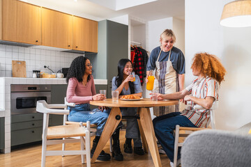 Fototapeta premium Four young multiethnic friends are sitting around a table in a modern kitchen, enjoying breakfast and conversation